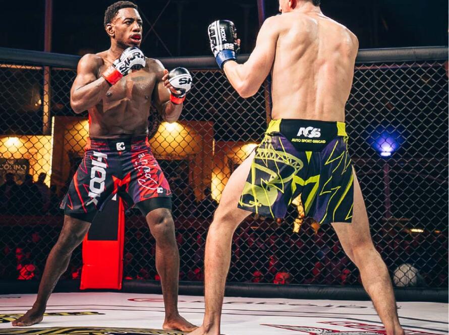 Luchadores de MMA en acción dentro de un octágono, uno con pantalones cortos rojos y el otro con pantalones cortos amarillos, listos para pelear en un evento deportivo.