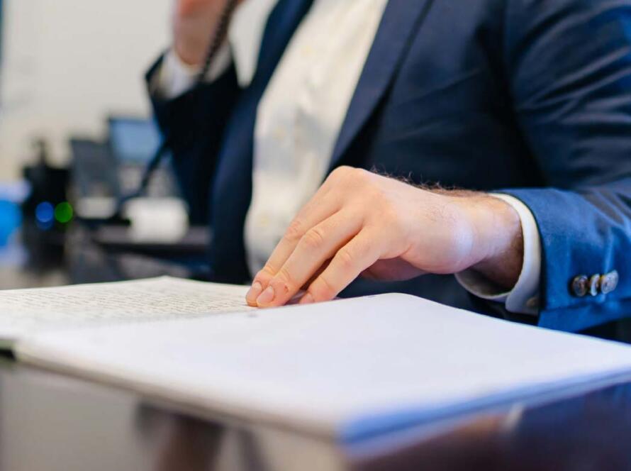 Hombre de negocios hablando por teléfono mientras toma notas en un cuaderno en su oficina, vestido con un traje azul.