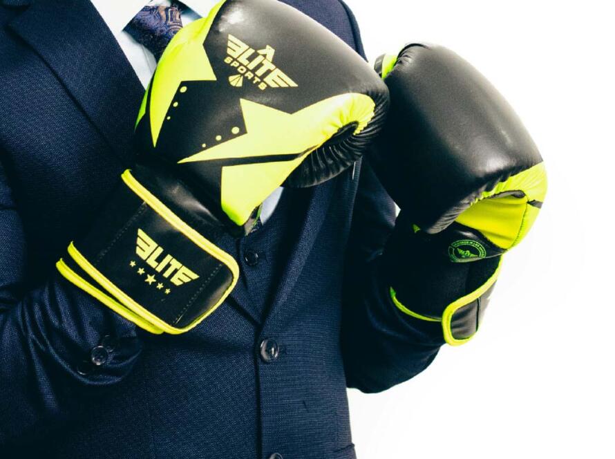 Hombre con guantes de boxeo negros y amarillos, vistiendo un traje elegante, preparado para un combate o entrenamiento de boxeo.