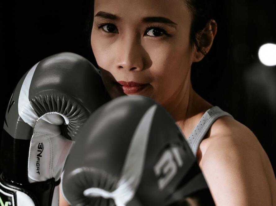 Mujer entrenando boxeo con guantes negros, mostrando concentración y determinación en un entorno oscuro.